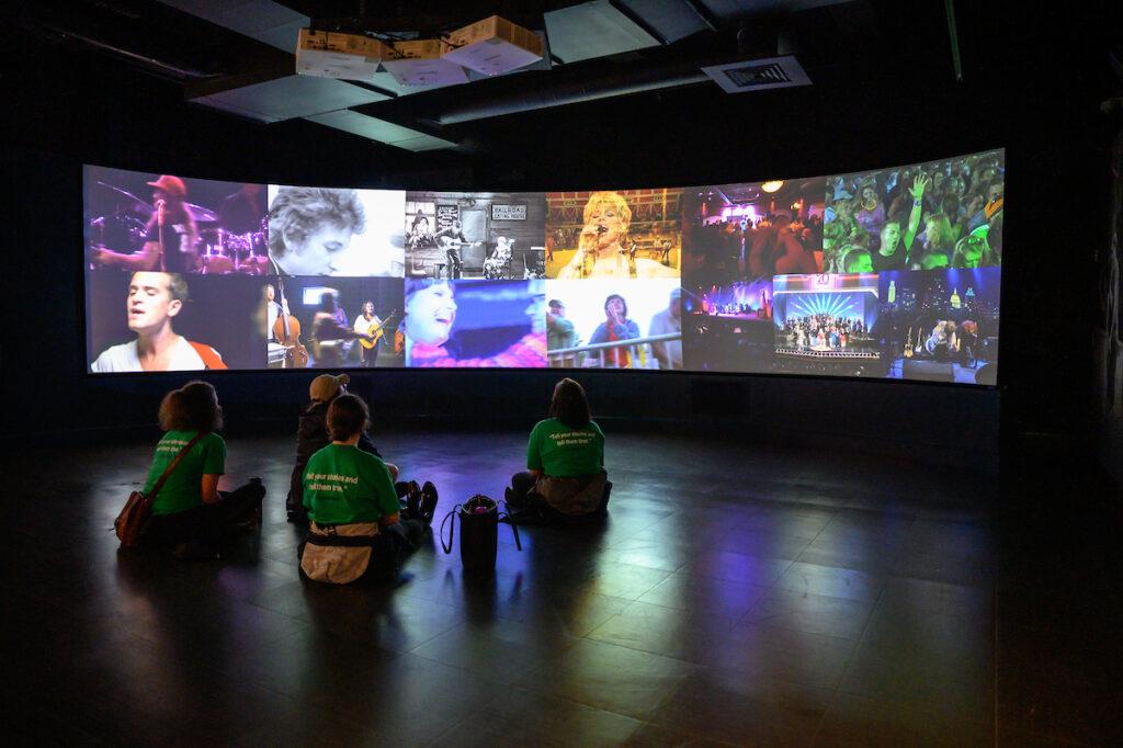 Tour participants sitting in a dark theatre looking at screens of country music stars